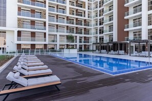 Ein modernes Hotel mit Pool auf dem Dach, Liegestühlen und einem mehrstöckigen Gebäude mit Balkonen.