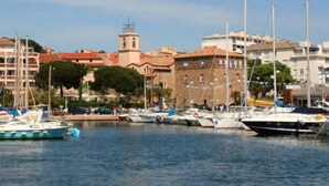 A marina with boats docked, a prominent building with a tower, and a clear sky. - Apartment with garden in Sainte-Maxime (Sainte-Maxime)