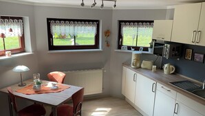 Une cuisine moderne avec des meubles blancs, une table à manger avec des chaises, une machine à café et une bouilloire.