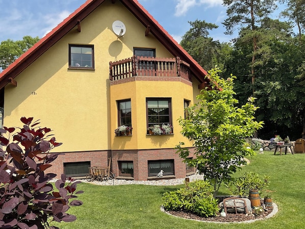 A yellow house with a red roof, a balcony with wooden railings, and a satellite dish. - Moderne Fewo in Ruhiger Lage am Radweg Gelegen mit Gartennutzung (Murchin)