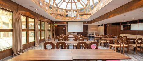 Ein Konferenzraum mit hoher Decke und großen Fenstern, Holztischen und -stühlen sowie einer Projektionsleinwand.