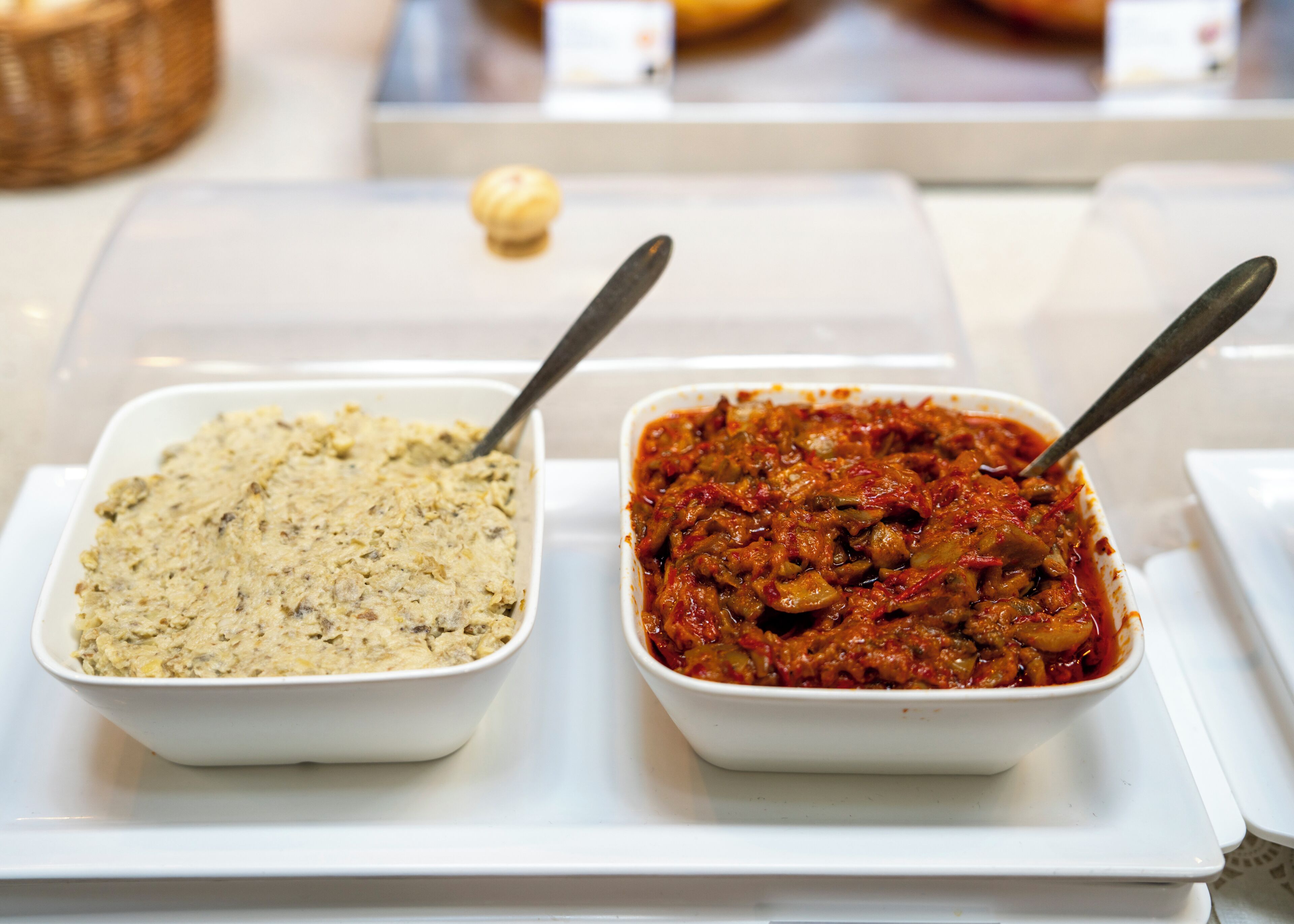 Two white bowls on a white tray, one with a creamy mixture and the other with a red sauce, both with spoons.