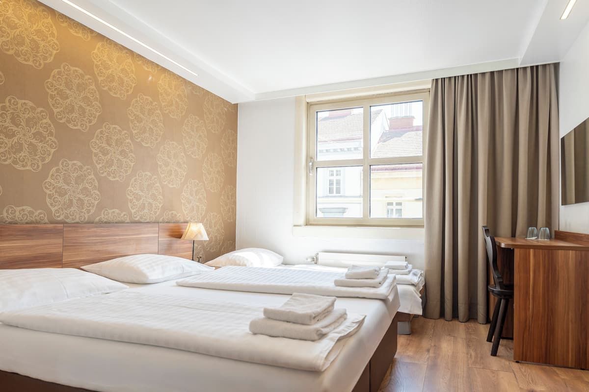 Habitación de hotel con dos camas, un escritorio, una silla, una lámpara y un ventanal con cortinas.