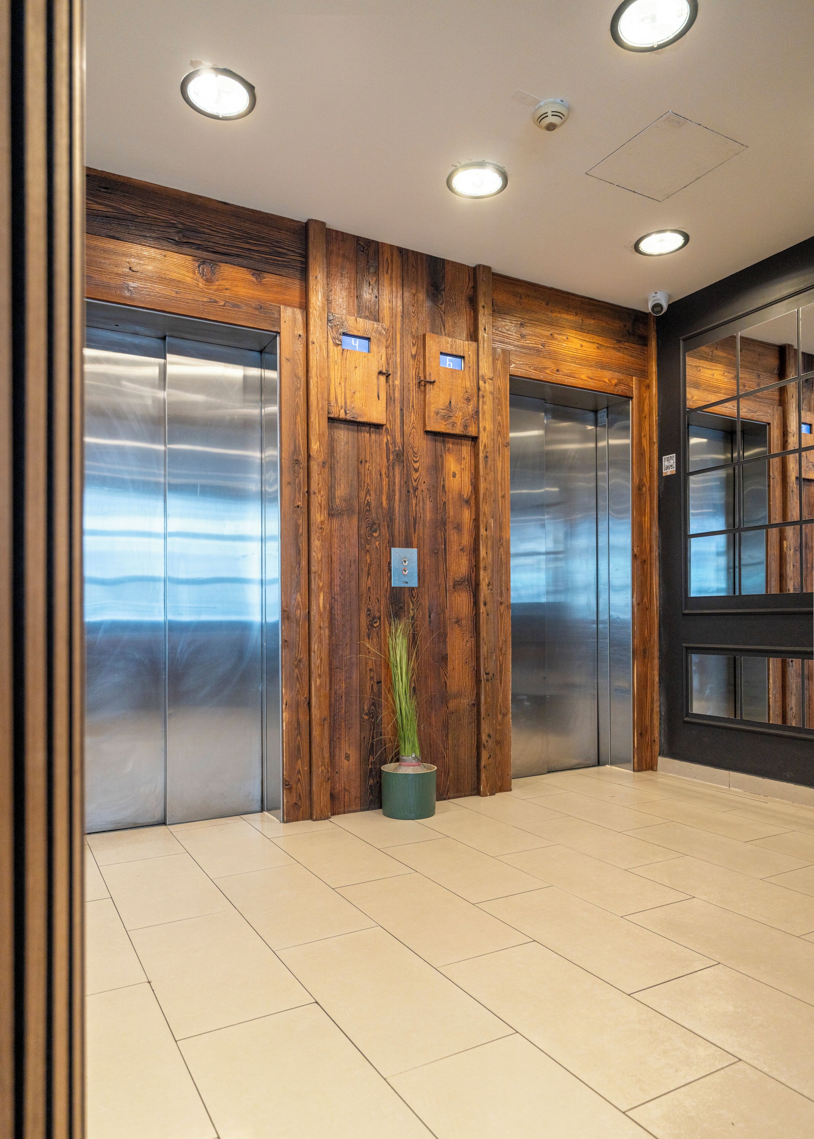 An elevator with wooden paneling and a potted plant, a tiled floor, and a ceiling with recessed lighting.