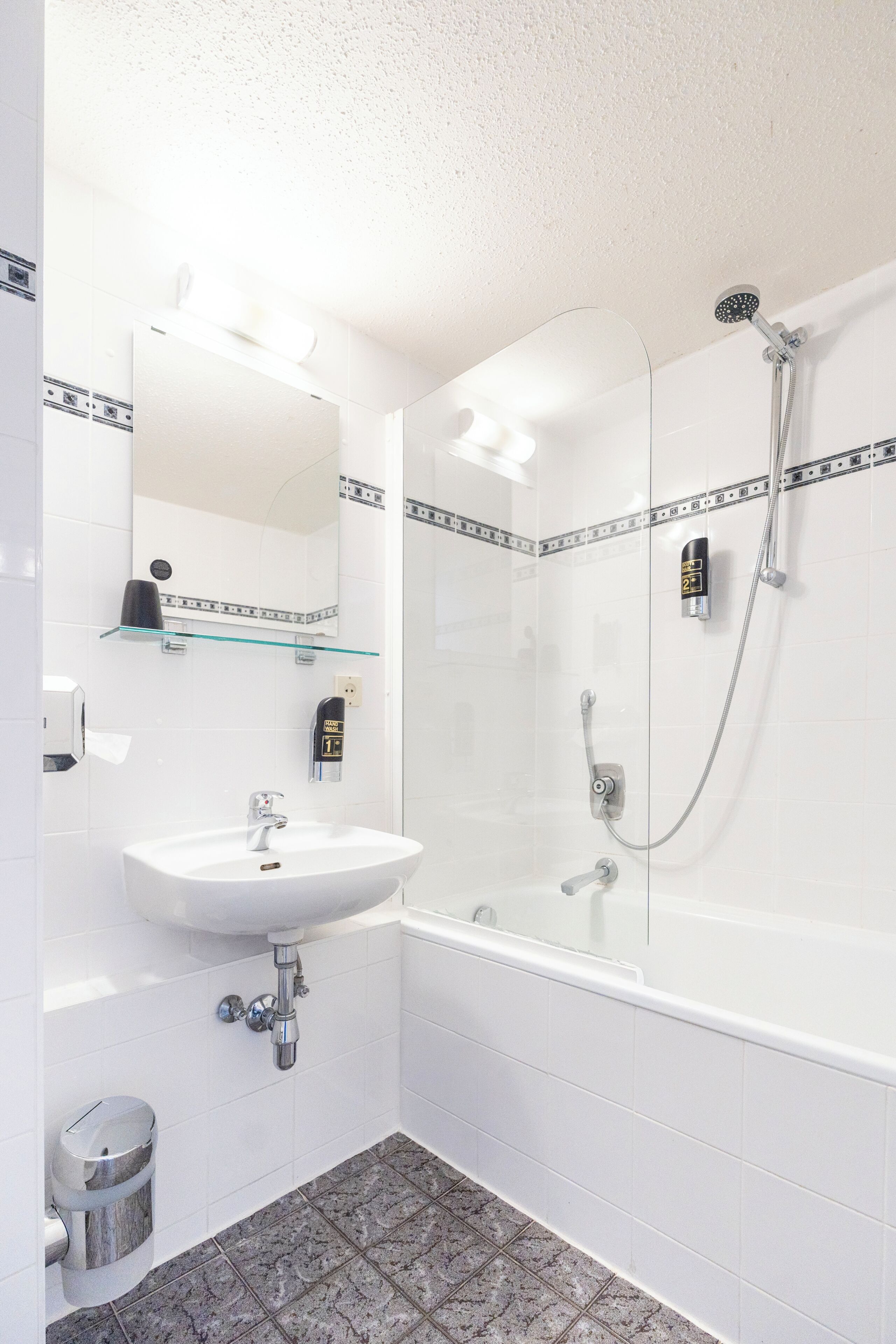 Een badkamer met een douchecabine van glas, een witte wastafel en een spiegel.