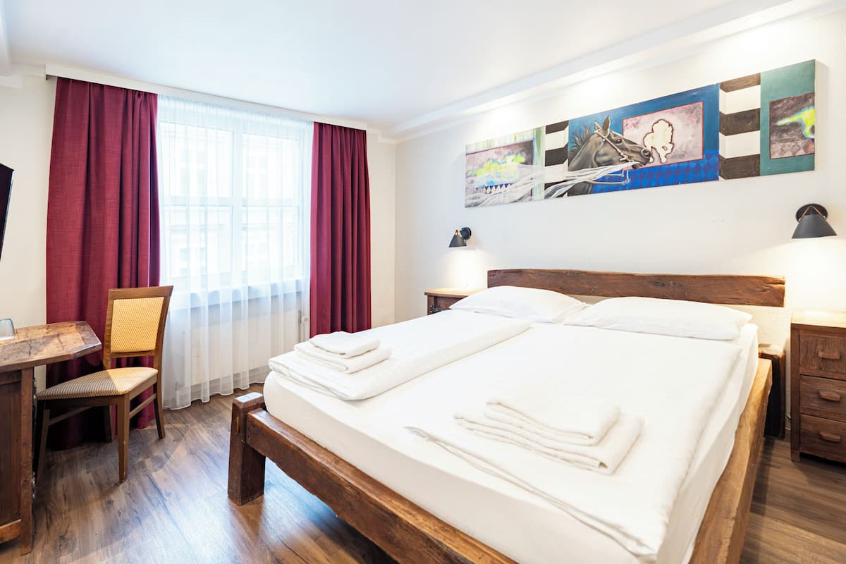 Una habitación de hotel con una cama de madera, un escritorio, una silla y obras de arte en la pared.