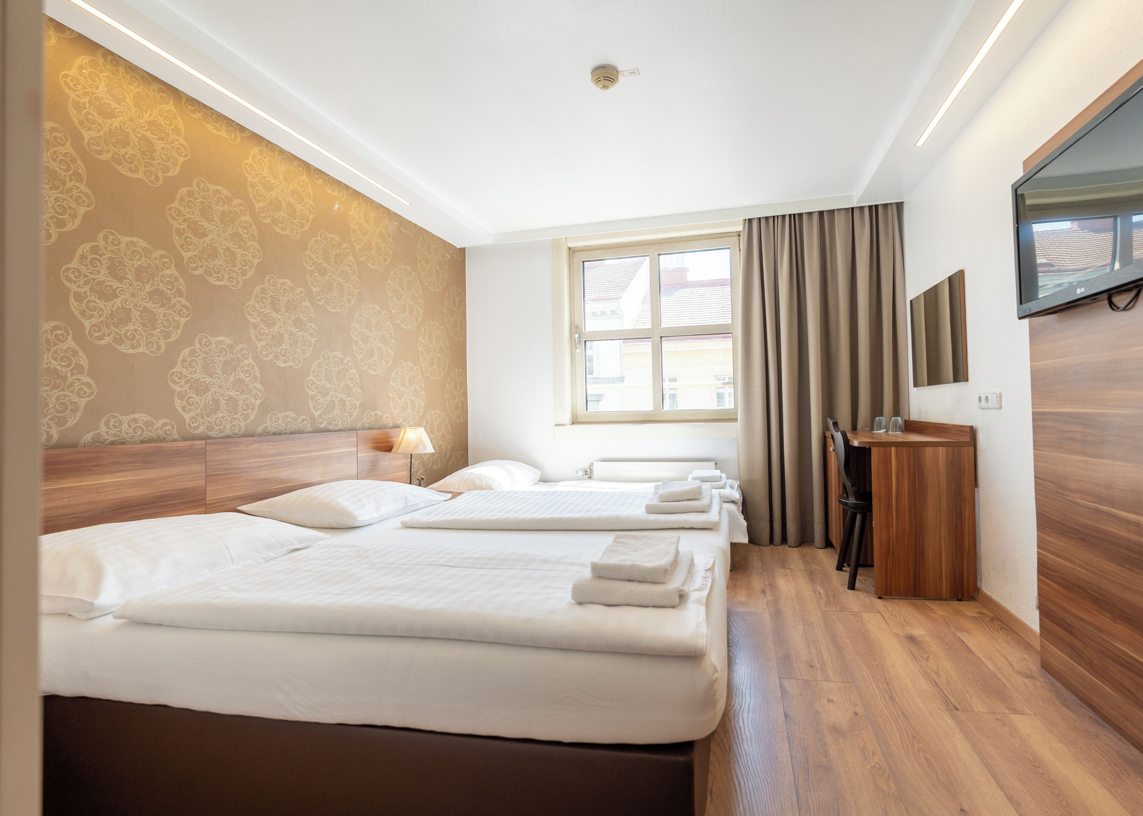 A hotel room with two beds, a desk, a TV, and a window with curtains.