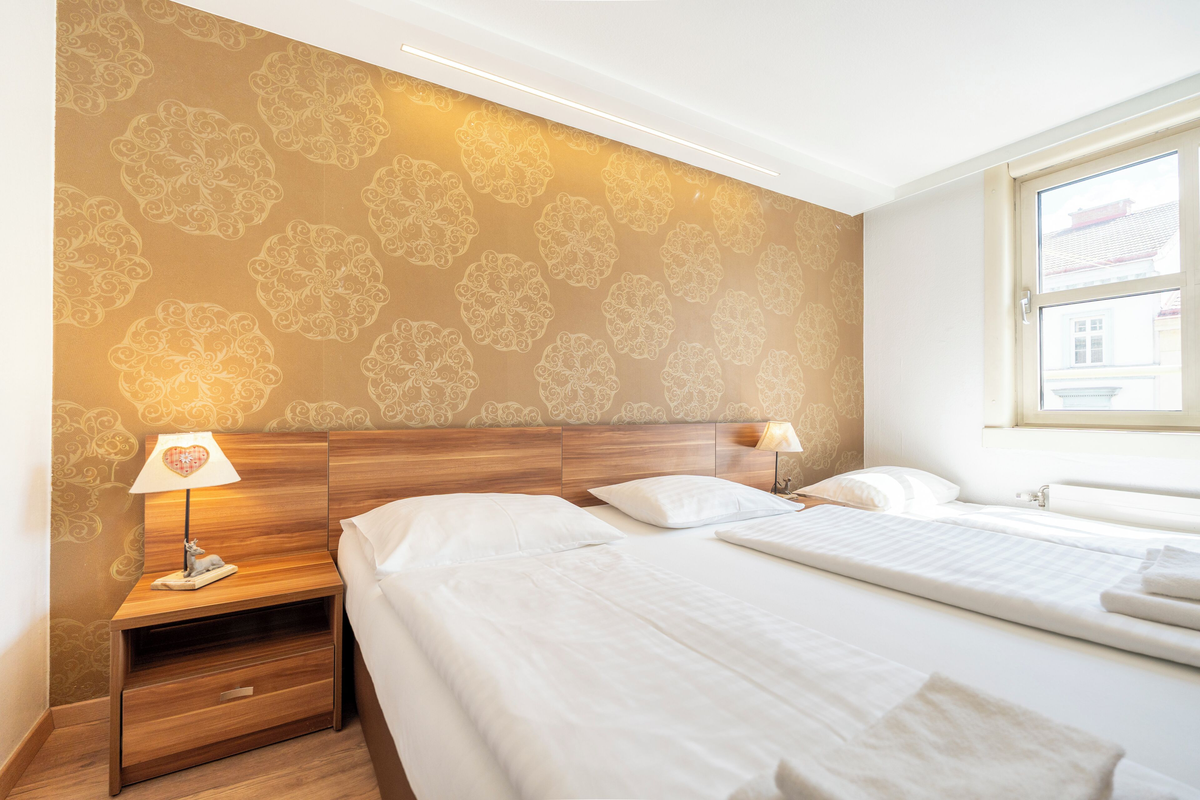 Een hotelkamer met een bed, nachtkastje, lamp en raam.