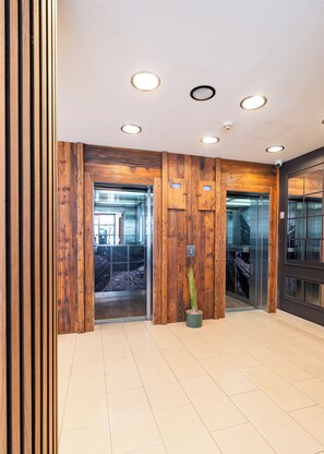 Een moderne lobby met houten lambrisering, een potplant en een lift.