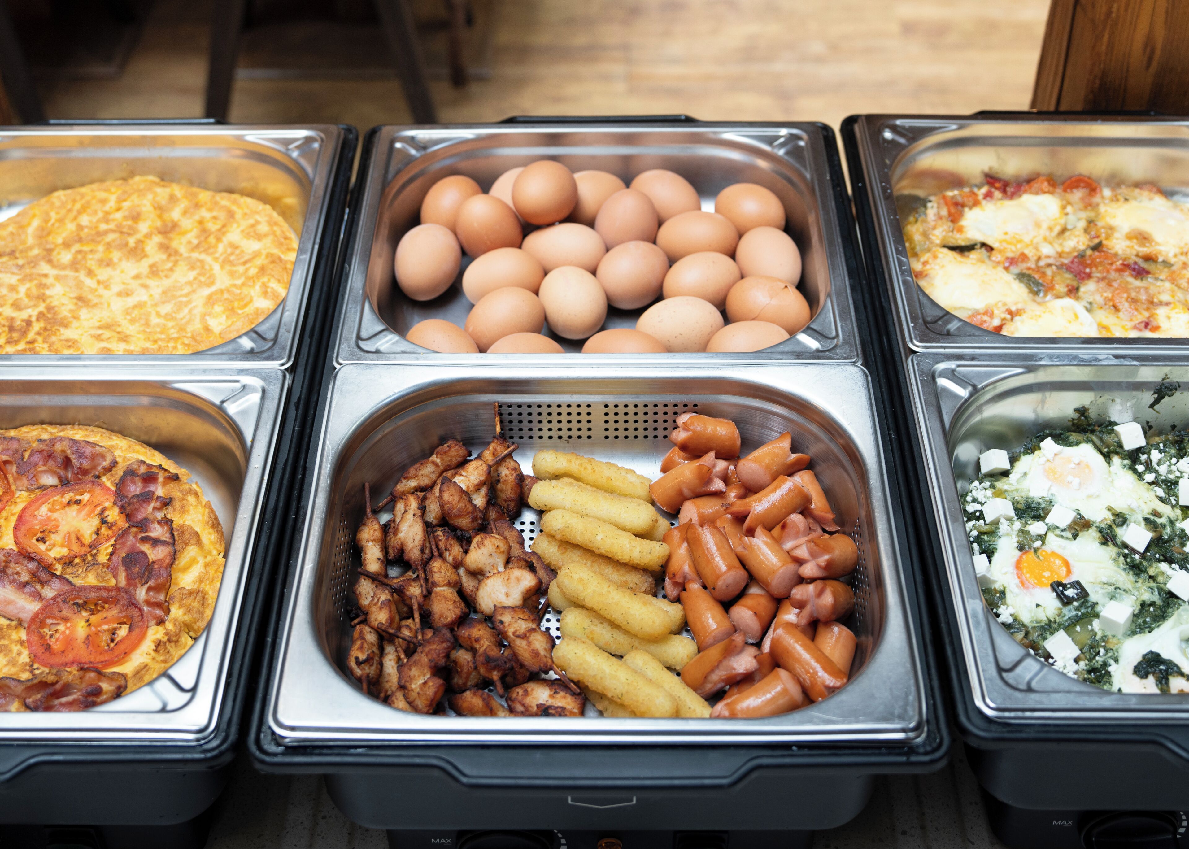 A buffet with various food options including eggs, sausages, and a dish with greens and cheese.