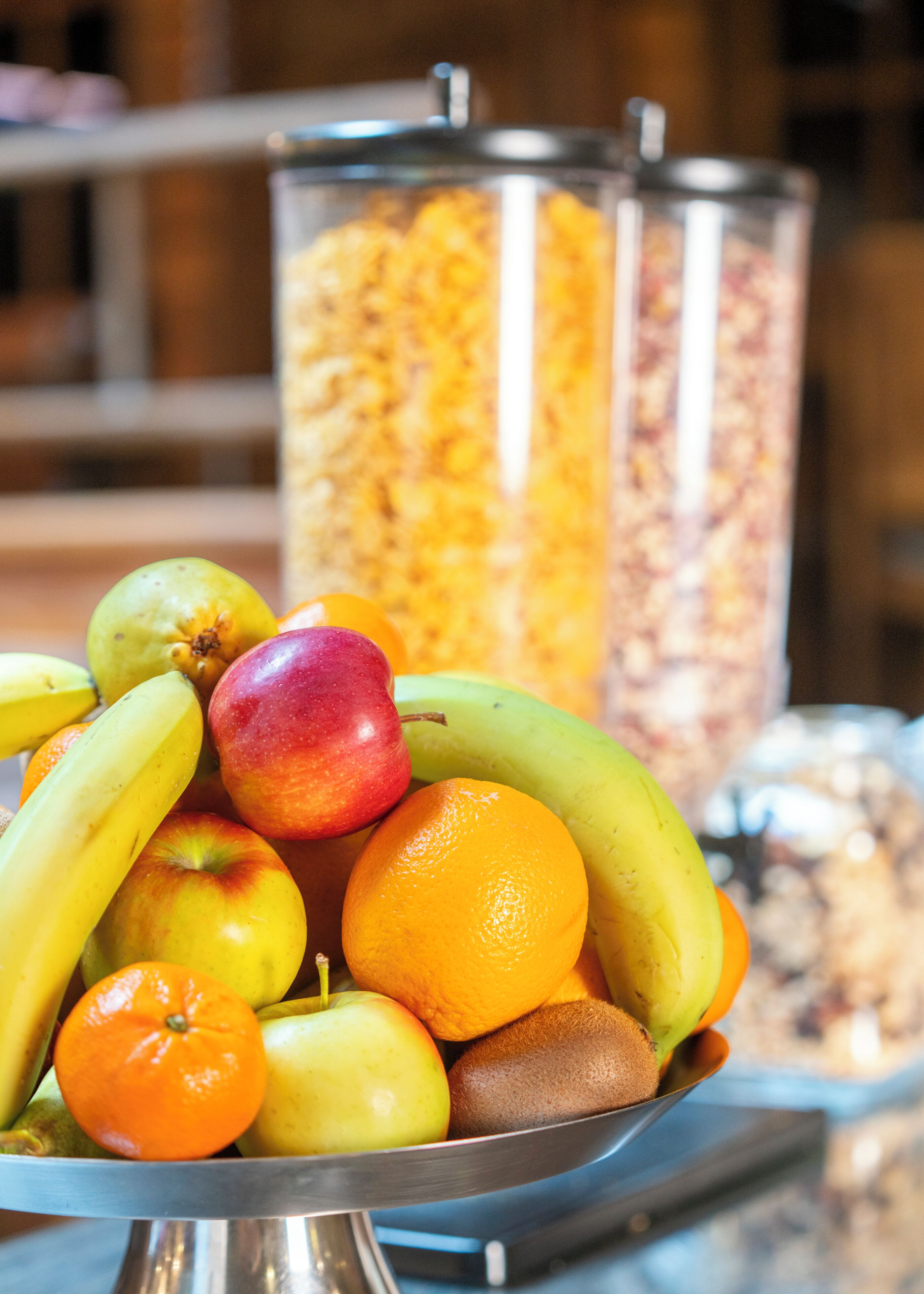 Un panier de fruits contenant des bananes, des pommes, des oranges et un kiwi, le tout disposé sur un plateau en métal.