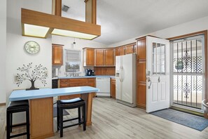 A kitchen with wooden cabinets, a white refrigerator, a sink, and a dining area with stools.