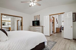 A bedroom with a large bed, a ceiling fan, a TV, and a dresser.