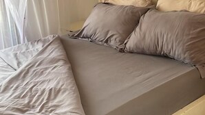 Una cama con estructura de madera y colchón gris, con dos almohadas.