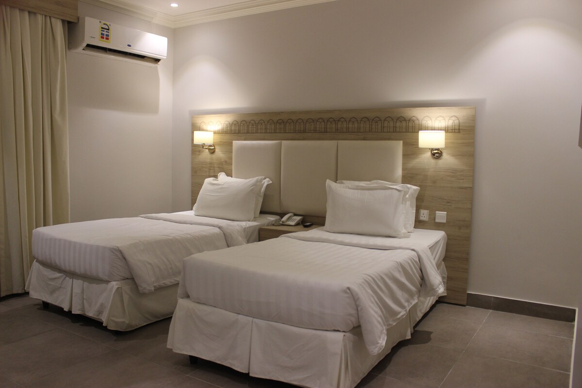 Habitación de hotel con dos camas, aire acondicionado montado en la pared y lámparas de noche.