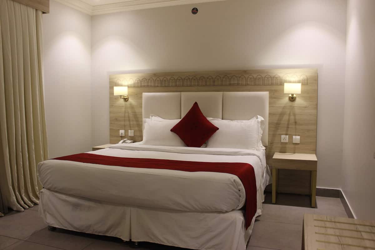 Una habitación de hotel con una cama grande, cabecera de madera, dos lámparas de noche y una mesita de noche.
