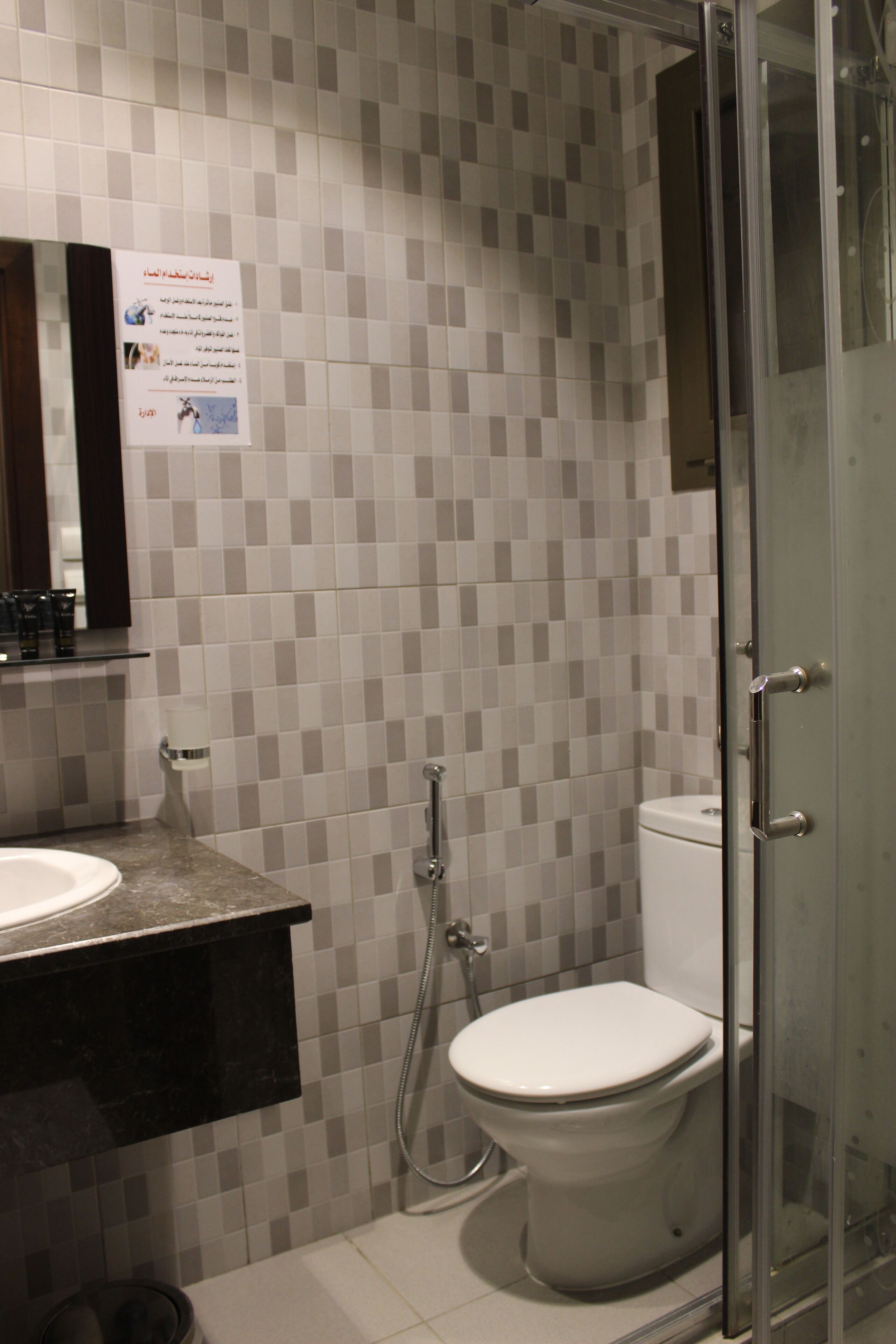 A bathroom with a tiled wall, a sink, a toilet, and a glass shower enclosure.