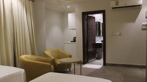 Een hotelkamer met twee bedden, een klein rond tafeltje en een gele fauteuil.