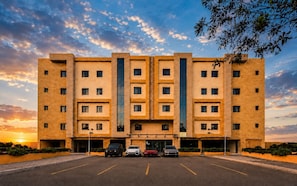Un immeuble à plusieurs étages, doté d’un parking à l’avant, qui présente un design architectural moderne avec un élément vertical central.