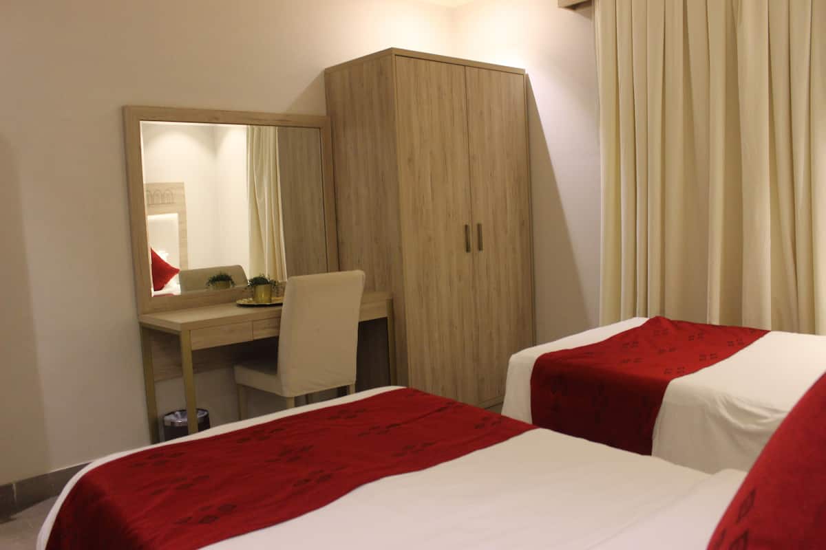 Habitación de hotel con dos camas, un escritorio, una silla y un armario.