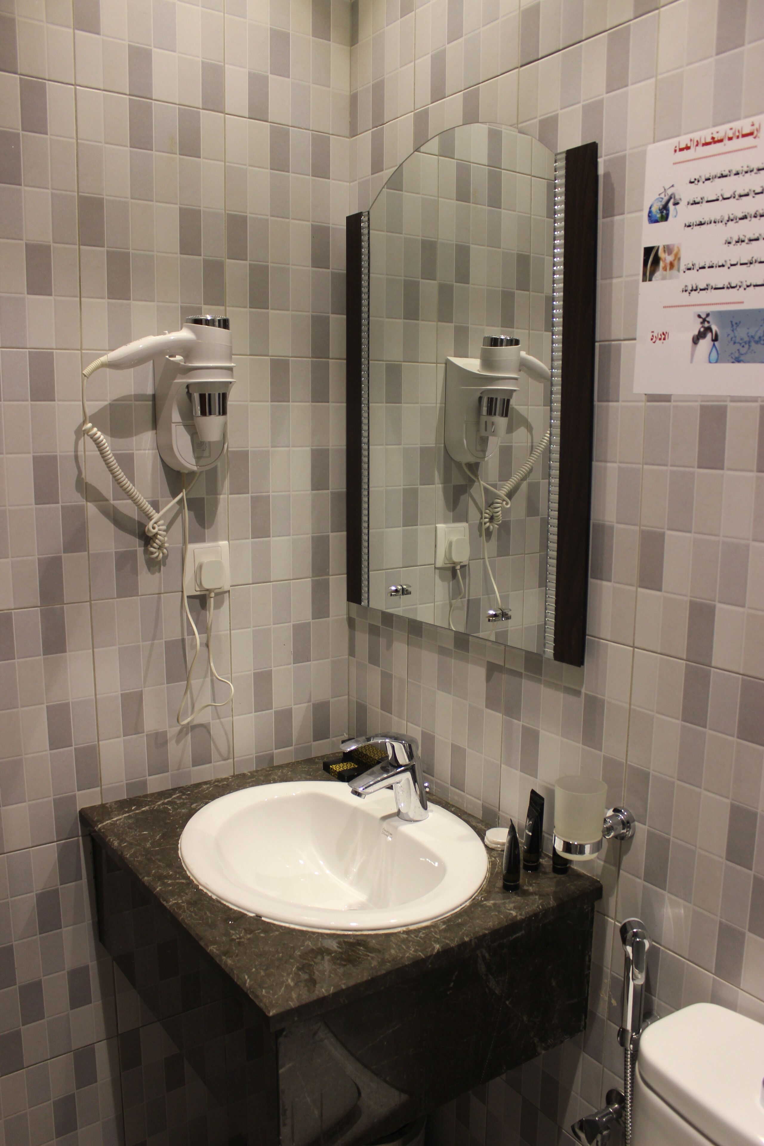 A bathroom with a white sink, a mirror, and a hairdryer mounted on the wall.
