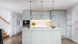 Eine moderne Küche mit einer zentralen Kochinsel, Pendelleuchten und einem eingebauten Backofen.