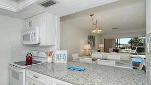 A modern kitchen with white cabinetry, a microwave, and a stove. There is a blue tray on the granite countertop. - Serene 1st floor 2 Bed 2 Bath Siesta Key Steps to Beach (Siesta Key)
