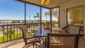 Un balcon avec une table et des chaises en verre, un ventilateur de plafond et une vue sur la plage et les palmiers.