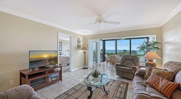 A living room with a television, a glass coffee table, a sofa, and a chair.