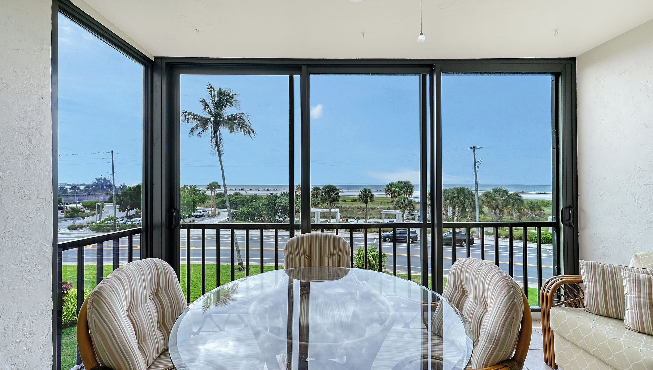 A balcony with a glass table and chairs, overlooking a road and palm trees.