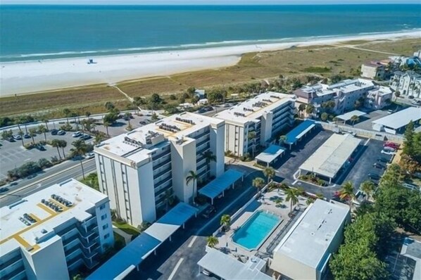 An aerial view of a hotel complex with multiple buildings, a parking lot, and a beach in the background.