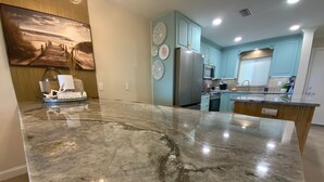 A kitchen with a large marble countertop, light blue cabinets, and a stainless steel refrigerator. - Coveted Siesta Key Escape 1 Bed 1 Bath with Gulf Views Steps to Beach (Siesta Key)