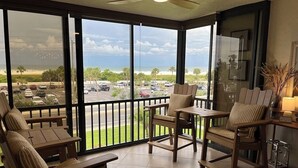 A sunlit room with large windows, a ceiling fan, and a view of a parking lot and beach. - Coveted Siesta Key Escape 1 Bed 1 Bath with Gulf Views Steps to Beach (Siesta Key)