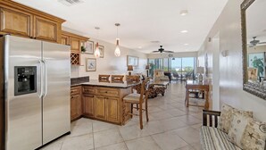 A spacious kitchen with wooden cabinets, a stainless steel refrigerator, and a dining area with a table and chairs. - Siesta Key Beach 1 Bed 1 Bath Condo Steps to Beach with Full Gulf Views (Sarasota)