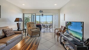 A living room with a sofa, armchair, TV, and a balcony with a view. - Siesta Key Beach 1 Bed 1 Bath Condo Steps to Beach with Full Gulf Views (Sarasota)