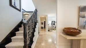 Una escalera con barandilla negra, peldaños alfombrados en tono beige y baranda de madera.