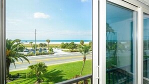 Blick vom Balkon auf einen Strand mit Palmen und einer Straße.