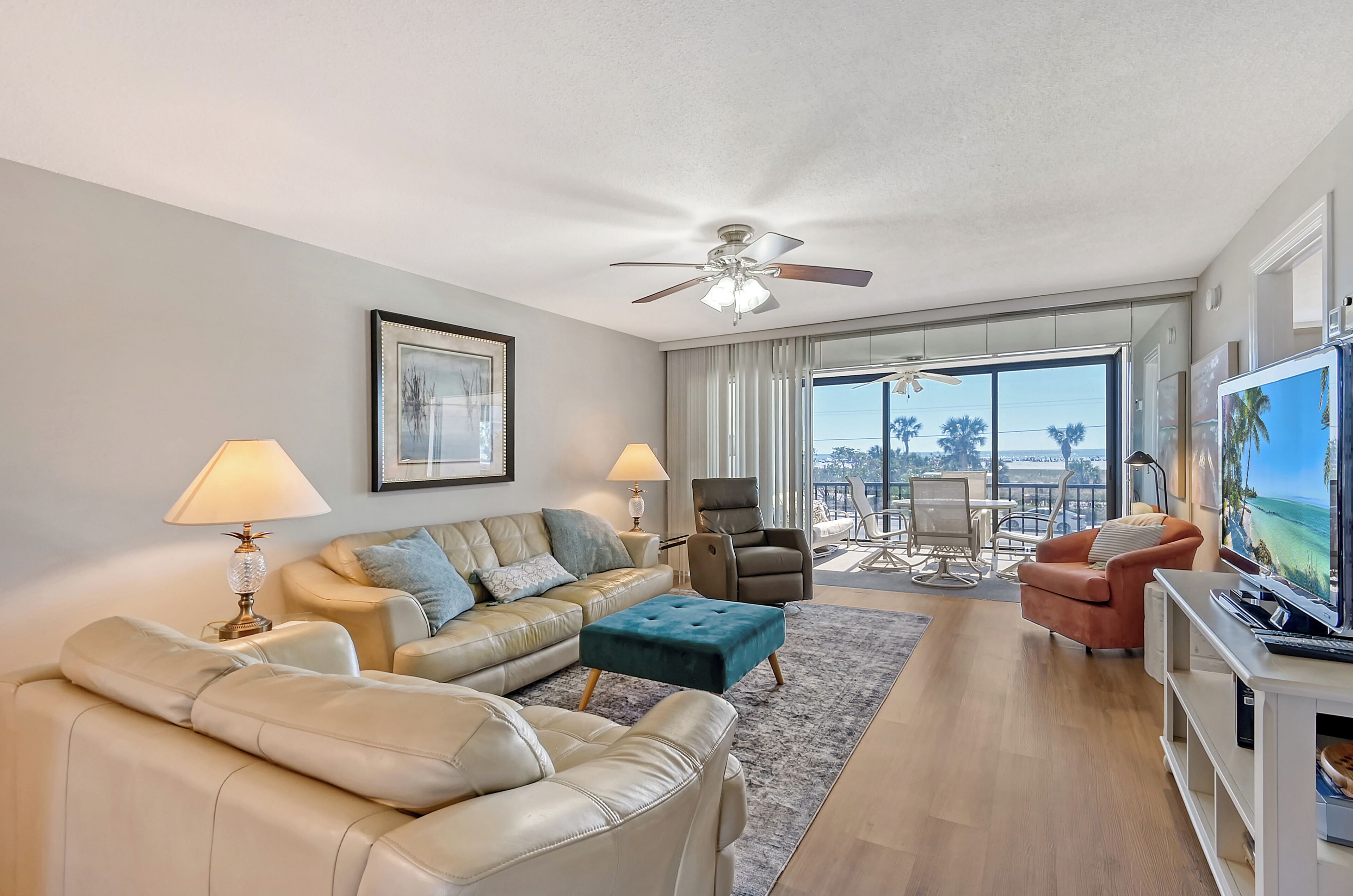 A modern living room with a sofa, ottoman, and armchairs, a ceiling fan, and a balcony with a view.