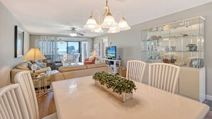 A modern living room with a dining area, a glass display cabinet, and a ceiling fan.
