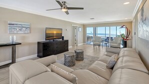 A spacious living room with a beige sofa, a black entertainment unit, and a ceiling fan.