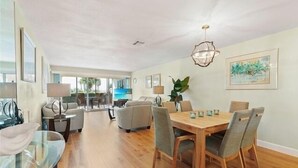 A spacious dining area with a wooden table and chairs, a glass coffee table, and a pendant light. - Siesta Key Beach 2/2 Ground Floor Steps to Beach (Sarasota)