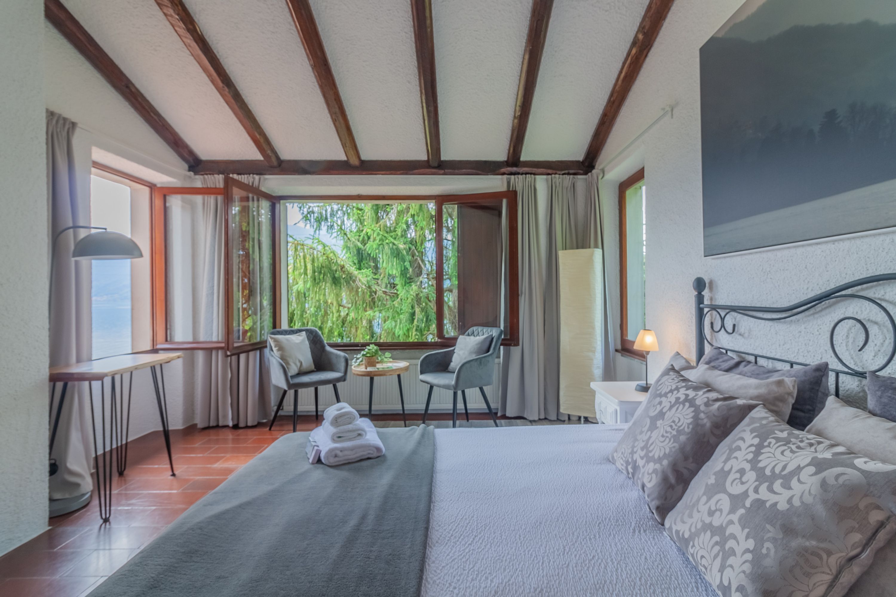 A hotel room with a bed, a desk, two chairs, a table, and a window with a view of greenery.
