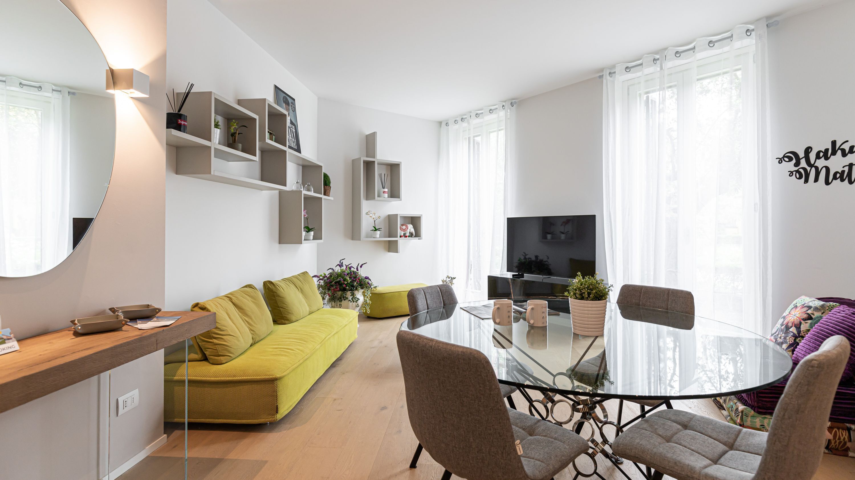 A modern living room with a glass dining table, a yellow sofa, and a TV.