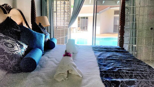 A bedroom with a bed, a nightstand, and a view of a swimming pool. - Jamaica Dream Villa - Iron Shore Escape (Montego Bay)