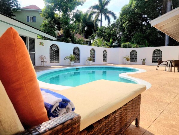Un espace aménagé au bord de la piscine, avec une chaise longue, un coussin et une petite table.
