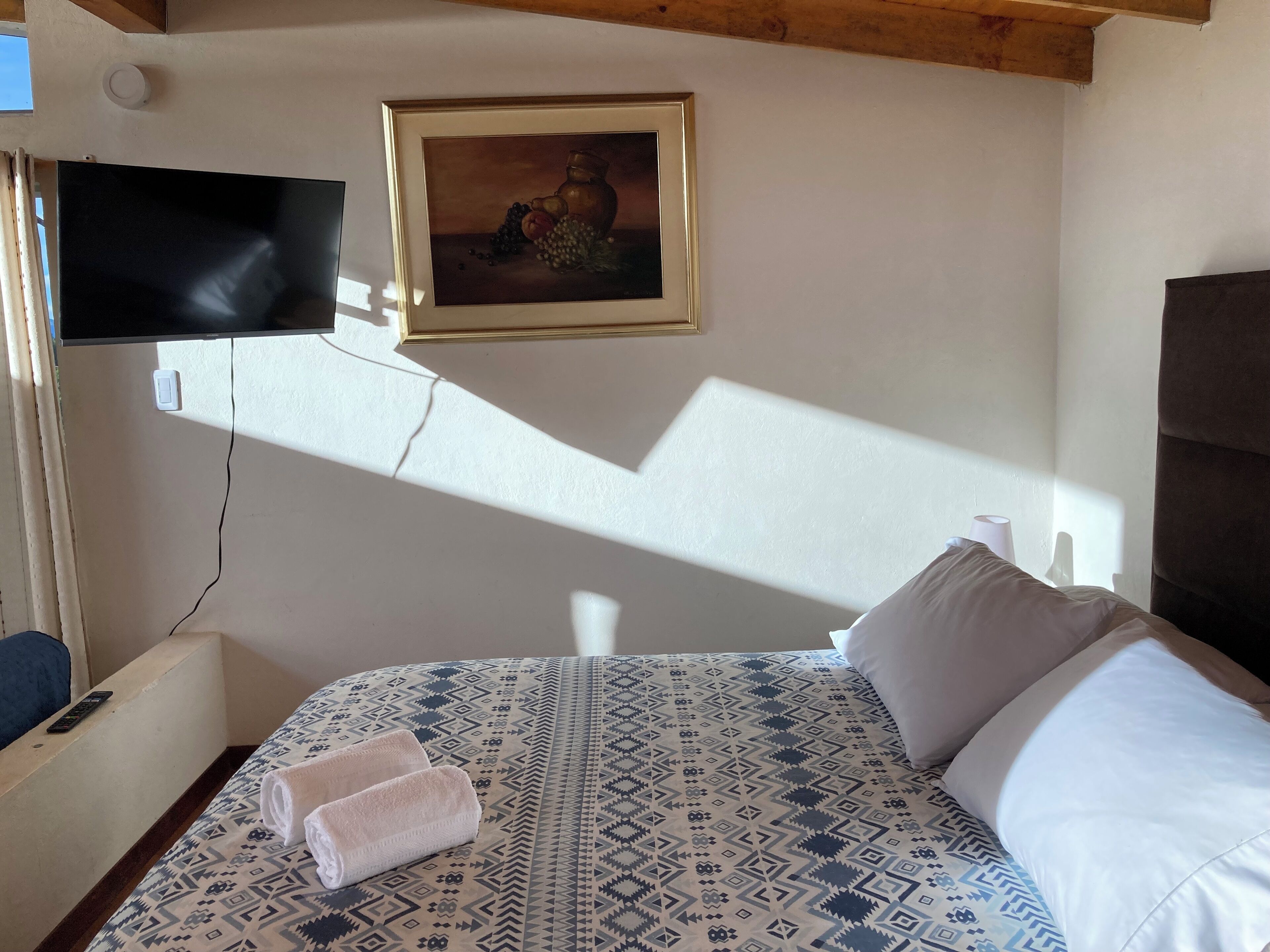 Een hotelkamer met een bed, een schilderij, een televisie en een raam dat schaduwen werpt.