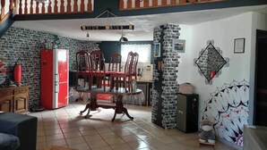 Un amplio salón con una mesa de comedor y sillas, un refrigerador rojo y una escalera que conduce a un nivel superior.