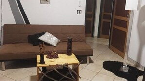 Una sala de estar con un sofá marrón, una mesita de madera con un florero y un adorno, y una alfombra negra.