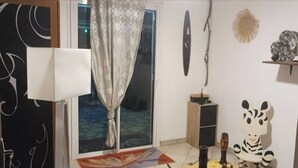 Una habitación con puerta corredera, ventana con cortina, una estatua de cebra y estante con adornos.