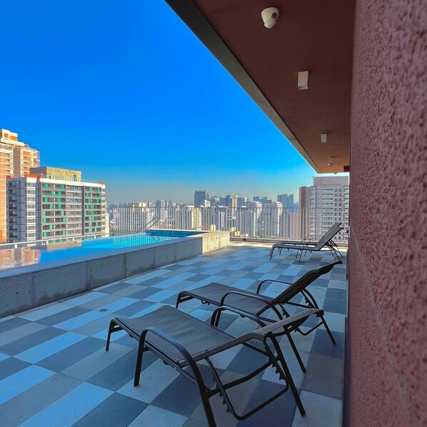 Eine Dachterrasse mit Pool, Liegestühlen und Blick auf den Stadtpanoram.